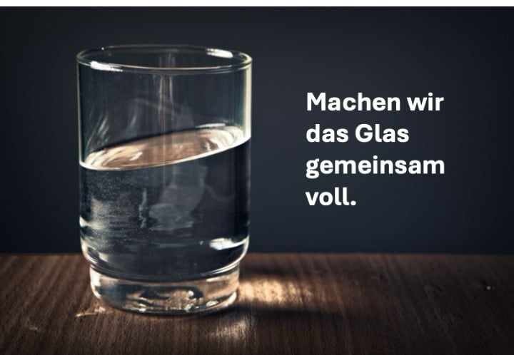 Halbvolles Wasserglas mit dem Schriftzug „Machen wir das Glas gemeinsam voll.“